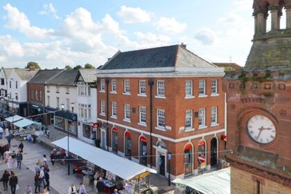 Overhead view of Ormskirk town center, featuring historic buildings, shops, and a bustling market square with pedestrians and local vendors.